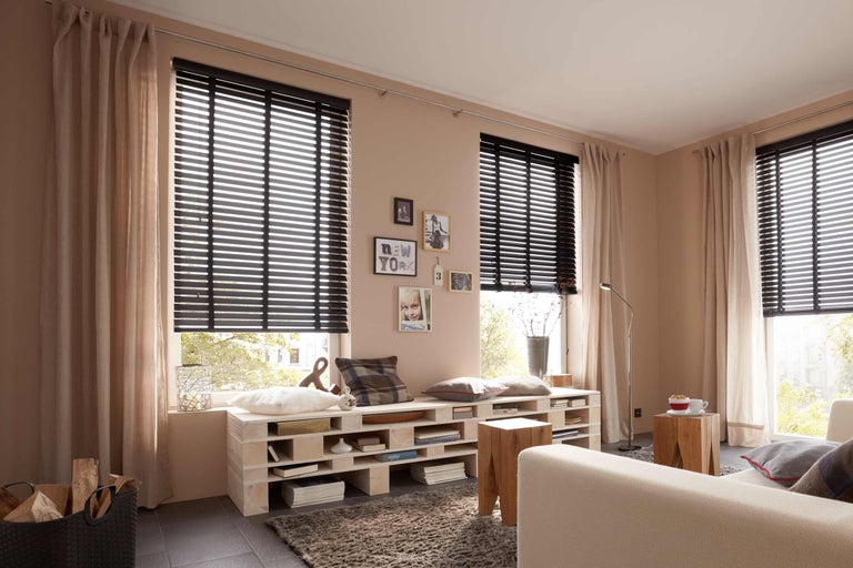 Woonkamer met houten jaloezieën, gordijnen en palletmeubilair