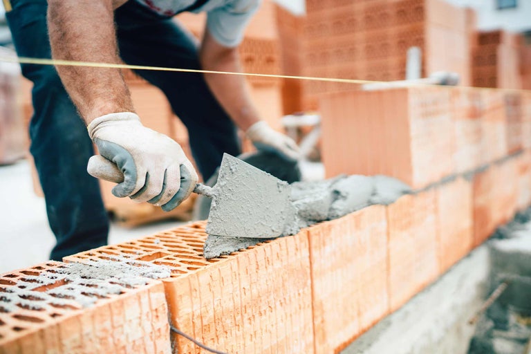 Metselaar die een bakstenen muur bouwt met mortel en een troffel