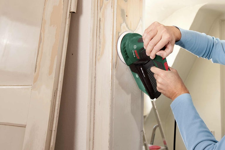 Een persoon schuurt een houten deur met een excentrische schuurmachine van Bosch.