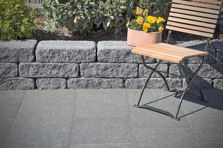 Tuinlandschap met stapelmuur, bestrating, bloemen en tuinmeubelen