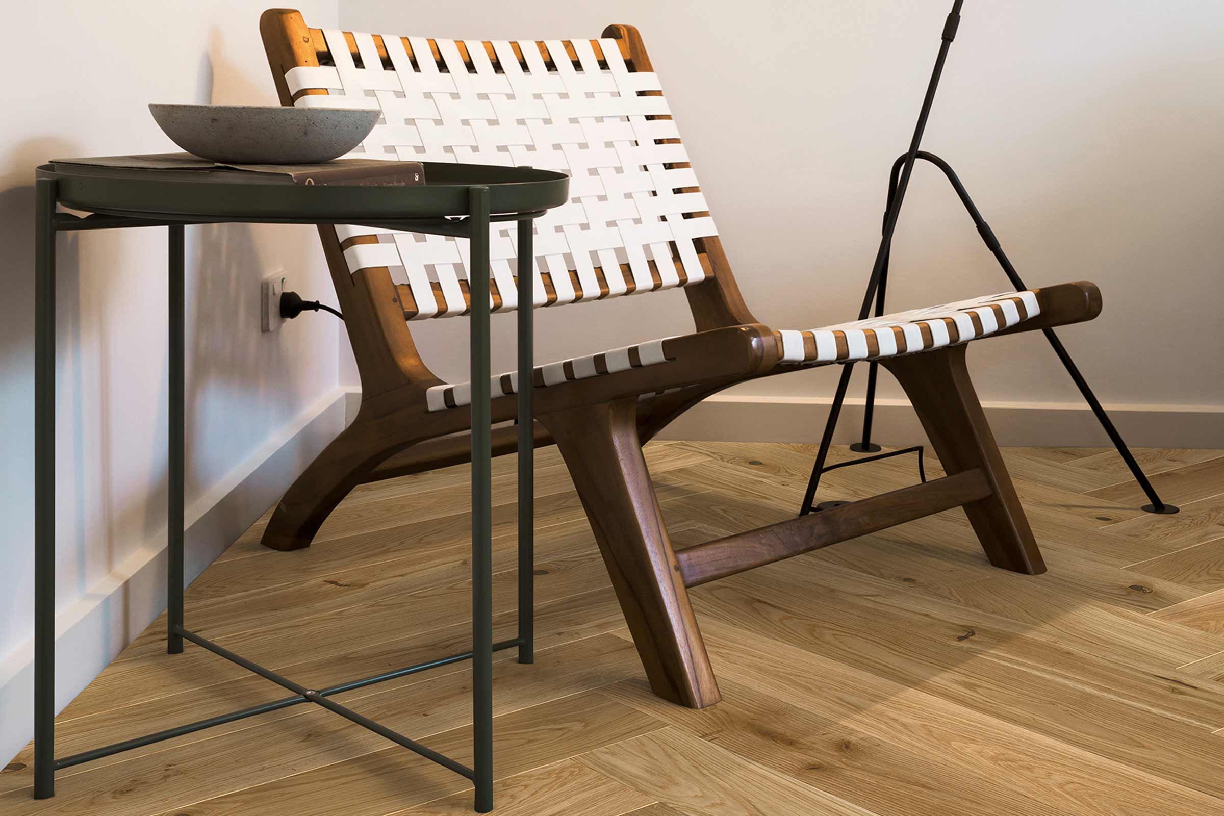 Interieurfoto met een fauteuil met houten frame en banden, een metalen bijzettafel en een staande lamp