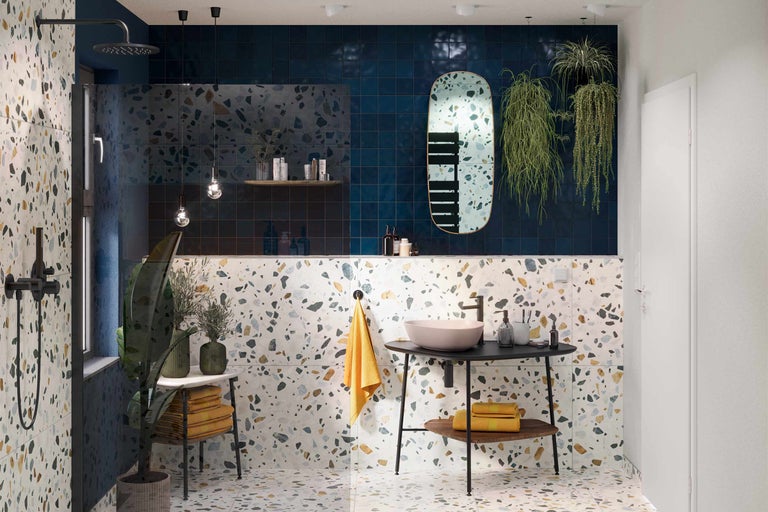 Lichte badkamer met terrazzo vloer, wastafel op een wastafelmeubel met handdoeken, douche en blauwe tegels