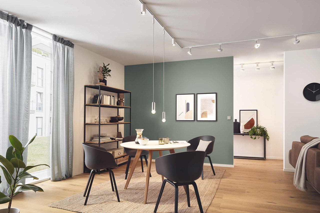 Lichte woonkamer met eettafel, stoelen, rekken, schilderijen en verlichtingssysteem
