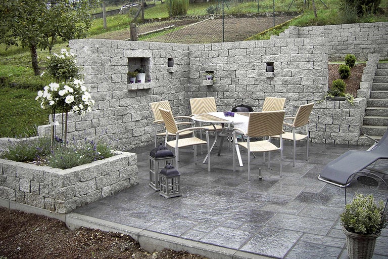 Aangelegde tuin met stenen muur, bestrating, tafel, stoelen en planten