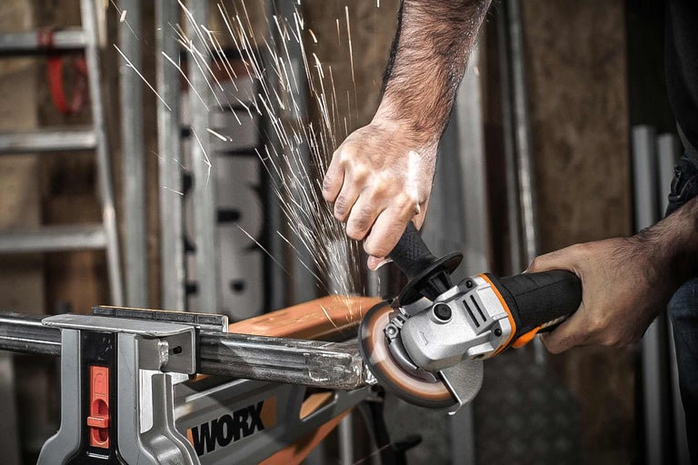 Een persoon gebruikt een haakse slijper met vonken om een stuk metaal te bewerken dat in een bankschroef is vastgeklemd.