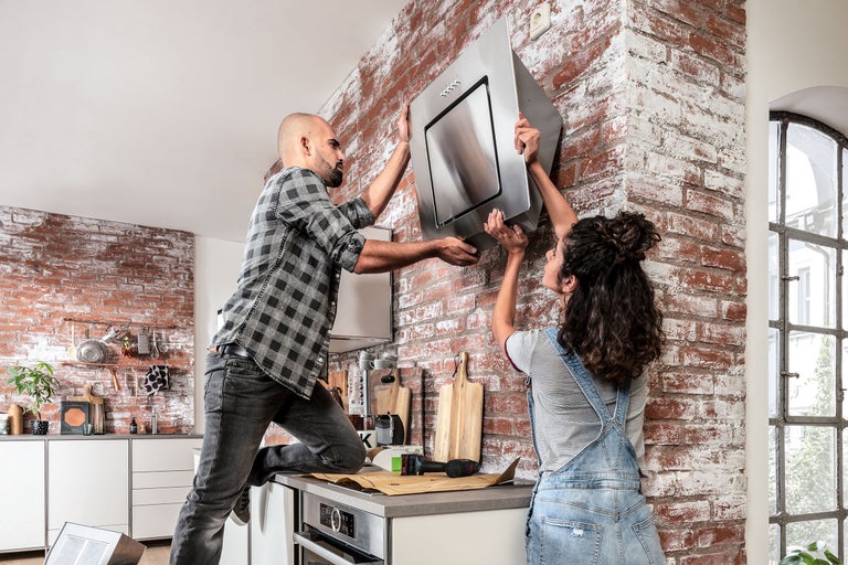 Twee mensen installeren een afzuigkap in een keuken met een bakstenen muur