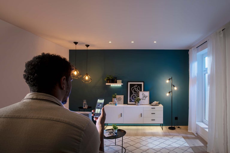 Man bedient verlichting in de woonkamer met een app op zijn smartphone