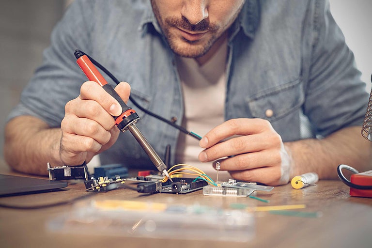 Man soldeert elektronische componenten met een soldeerbout op een printplaat.