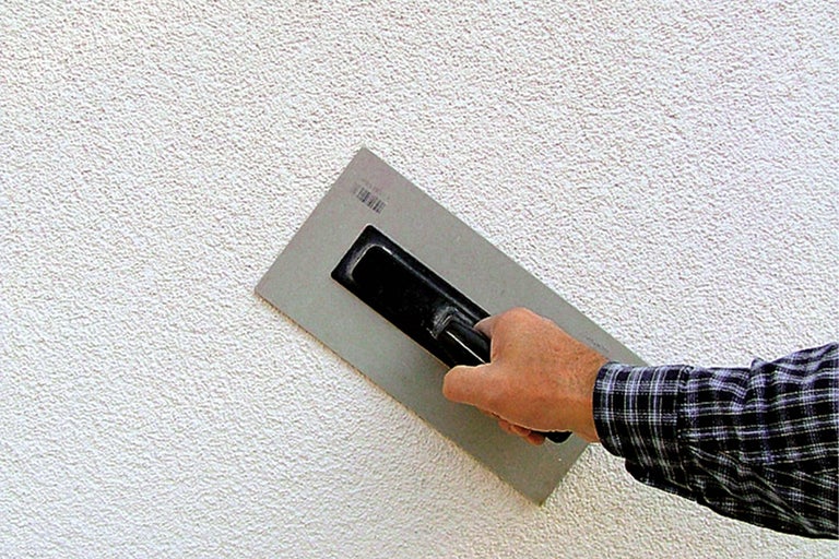 Buitenmuur met stucwerkstructuur en vakman met pleisterspaan