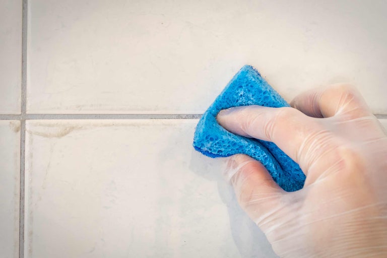 Een persoon met handschoenen reinigt tegels met een spons