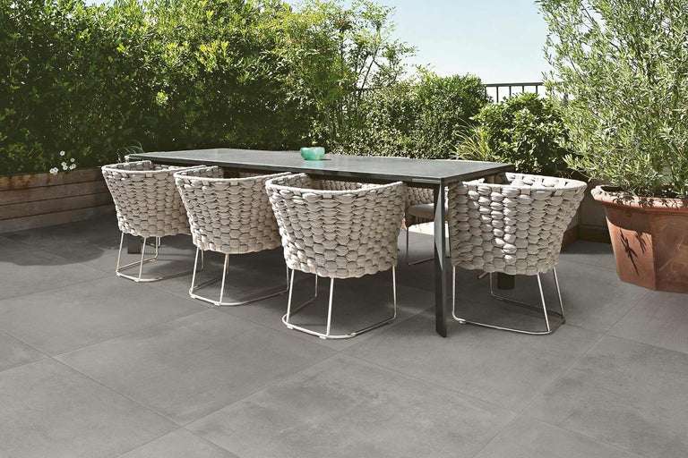 Eettafel met gevlochten stoelen op grijze terrastegels in de tuin