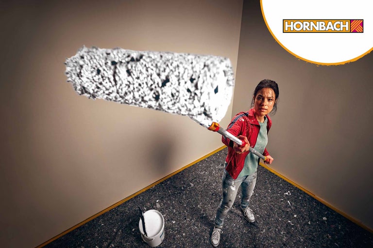 Vrouw schildert een muur met een verfroller, emmer verf staat in de kamer, Hornbach logo