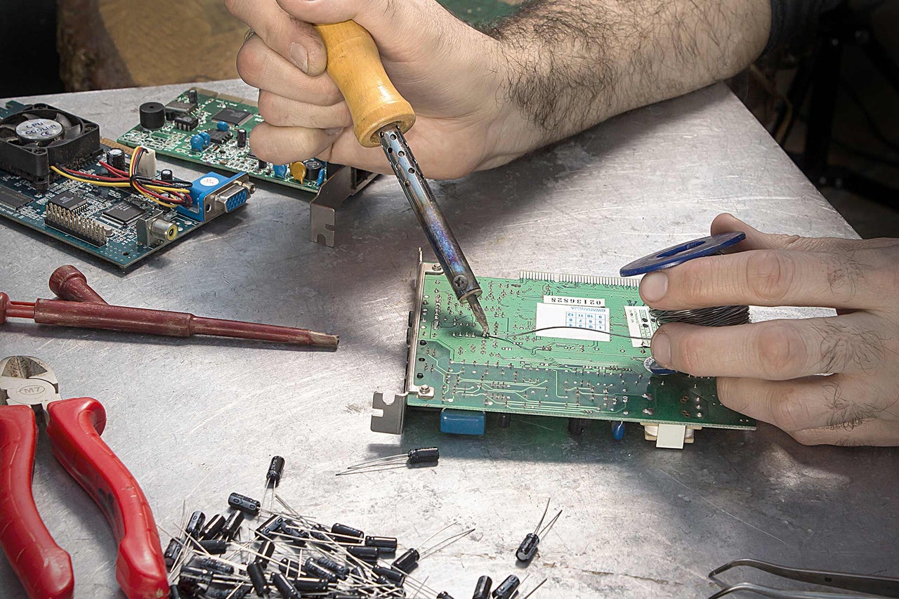 Elektronische printplaat solderen met soldeerbout en soldeertin op een werkbank.