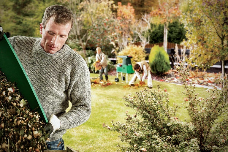 Tuinwerk scène met man, hakselaar en tuinafval in de herfst