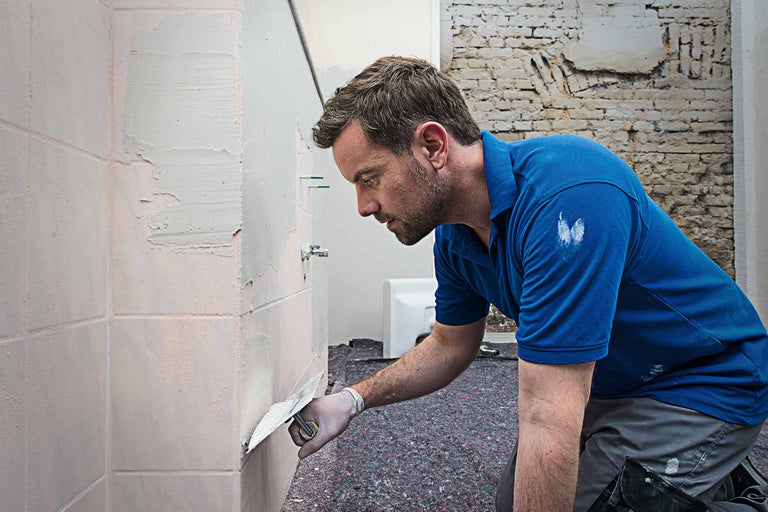 Een man plakt tegels in de badkamer.