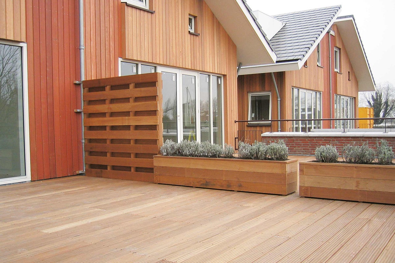 Houten terras met privacyscherm en beplante bloembakken voor een huis