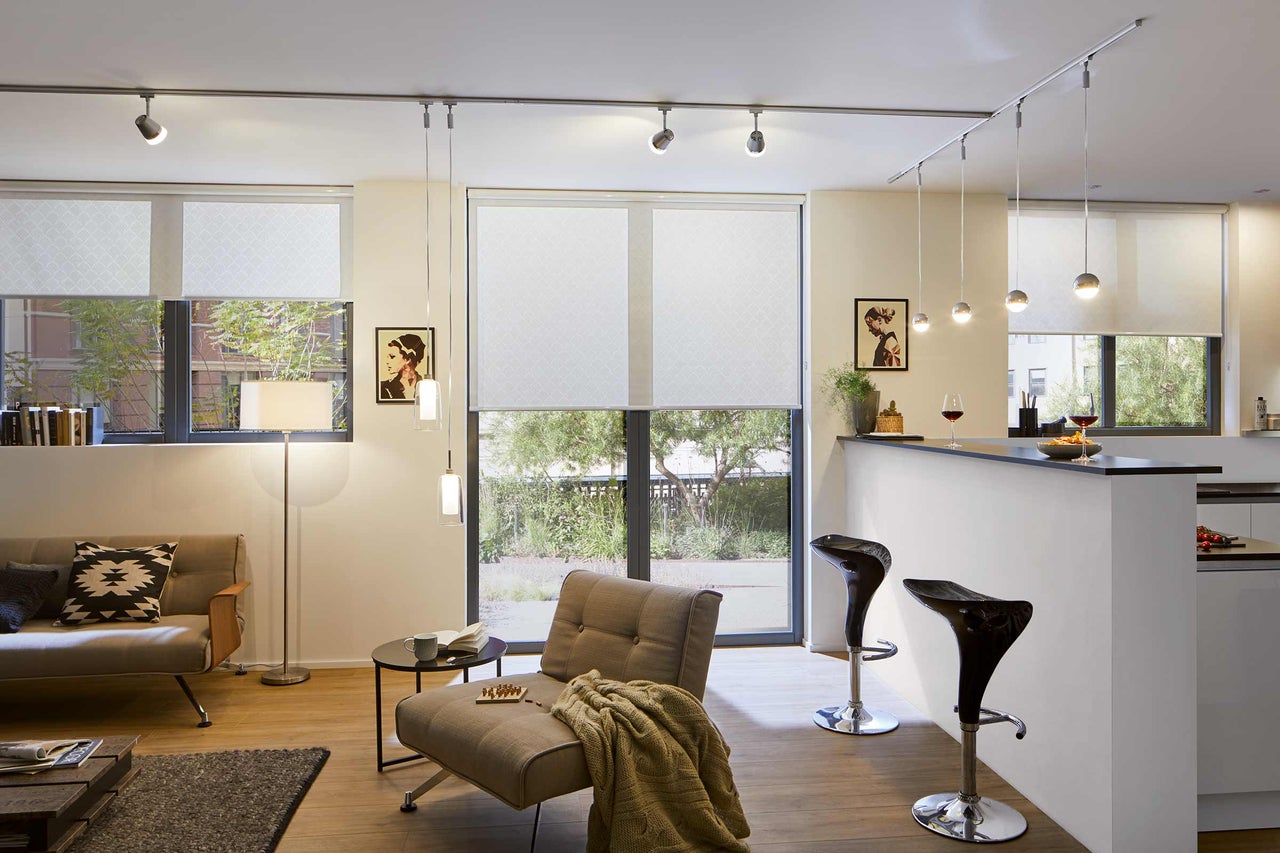 Woonkamer met bank, fauteuil, bar, plafondlamp en rolgordijnen