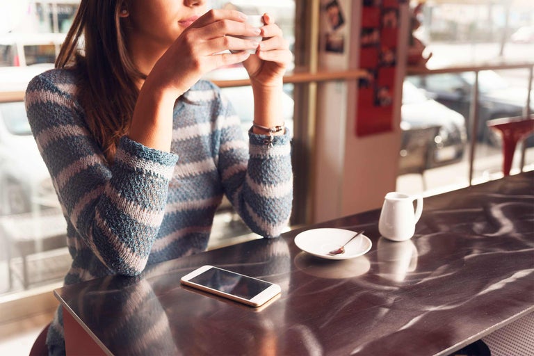 Vrouw drinkt koffie in een café met een smartphone op tafel