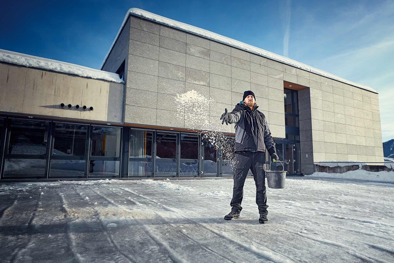Man strooit strooizout voor een gebouw op een ijzige ondergrond
