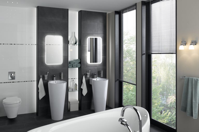 Lichte badkamer met twee wastafels op zuil, verlichte spiegels en ligbad