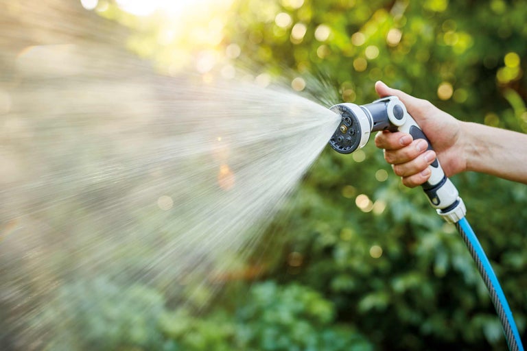 Een hand houdt een tuinspuit vast waar water uit komt