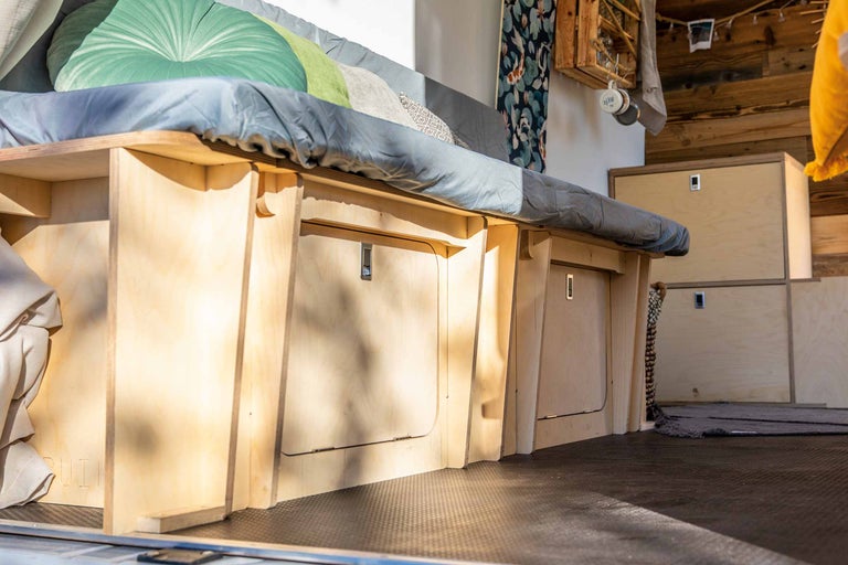 Interieur van een bestelwagen met bed, opslagruimte en houten lambrisering