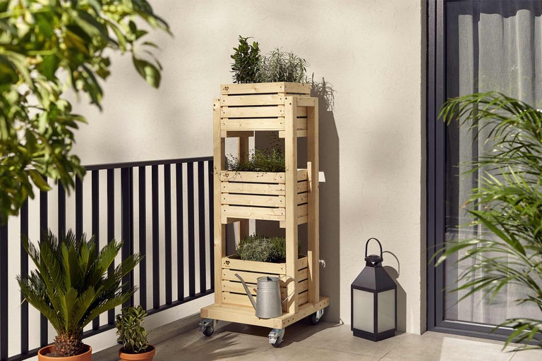 Houten plantenrek met drie niveaus en wielen voor op het balkon met gieter en lantaarn