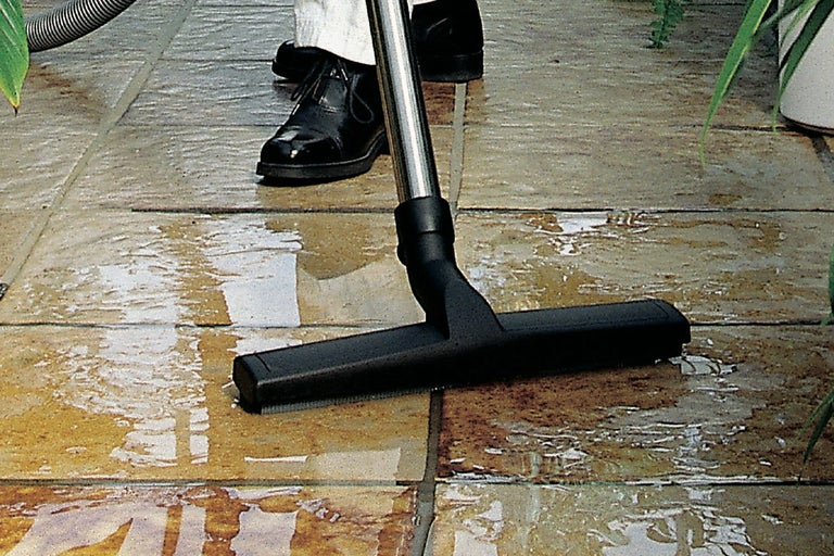 Iemand gebruikt een nat- en droogzuiger op een betegelde vloer.