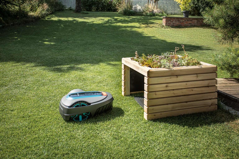 Tuinscene met robotmaaier en houten plantentafel.
