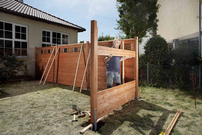 Een persoon bouwt een houten tuinafscheiding in de tuin.