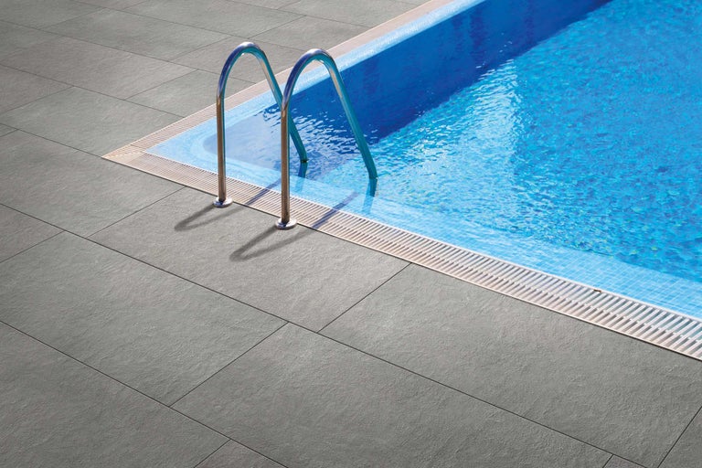 Grijze terrastegels naast een zwembad met een ladder.