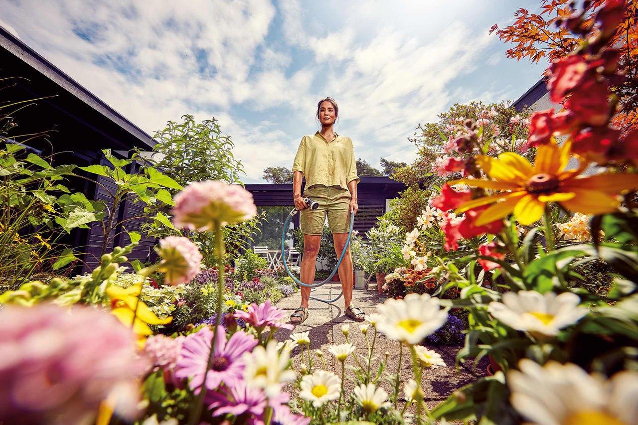 Vrouw sproeit bloemen in de tuin met een tuinslang.