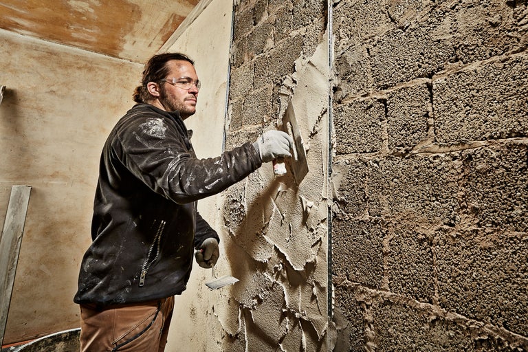 Ambachtsman pleistert een bakstenen muur met een troffel.