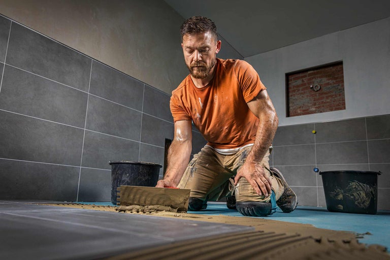Tegelzetter aan het werk: Tegels leggen met een spaan en emmer in een badkamer.