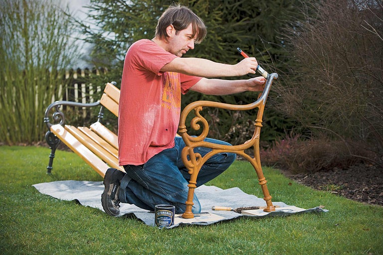 Man schildert tuinbank met metaalbeschermingslak in de tuin