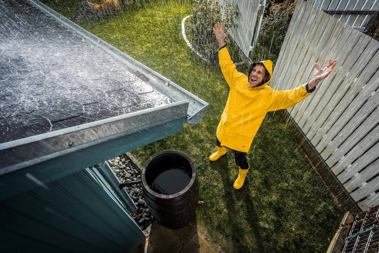 Scene met regenton, huisdak en persoon in regenkleding tijdens regenachtig weer