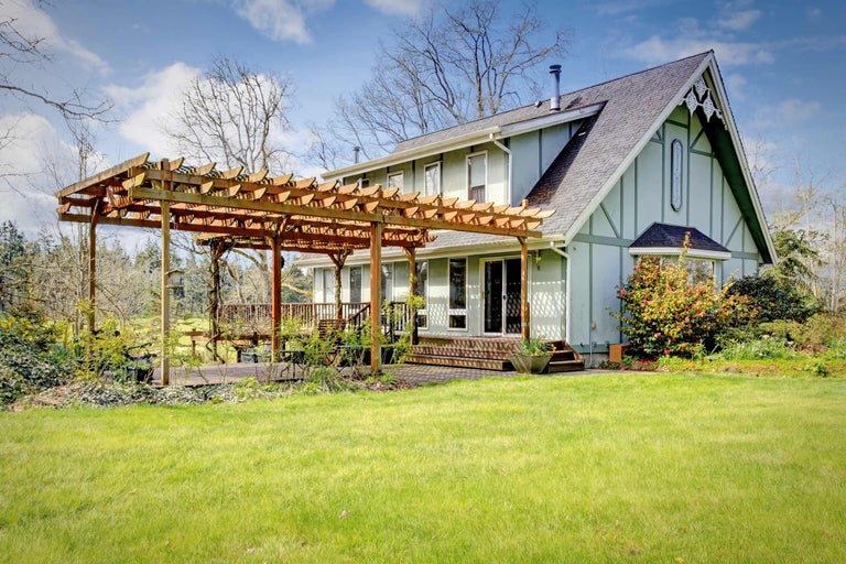 Een huis met een houten pergola, terras en gazon.