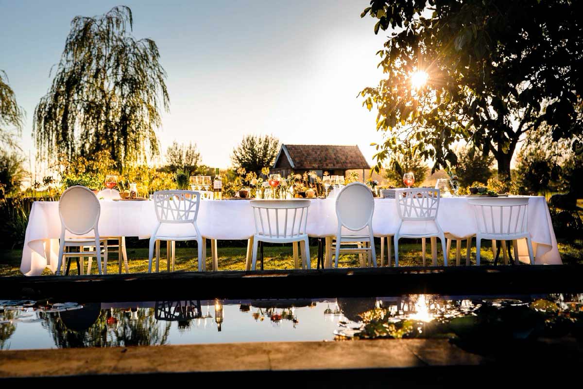 Buitenscène met een lange, witte tafel, gedekt met stoelen voor een tuinfeest