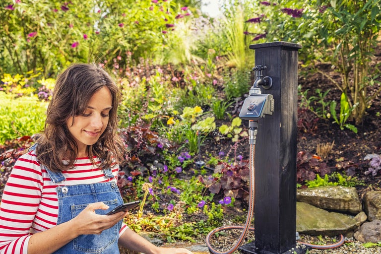 Vrouw met smartphone voor tuin met kraan en irrigatiebesturing