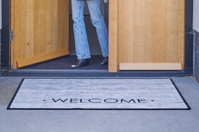 Deurmat met welkom tekst voor een open houten deur