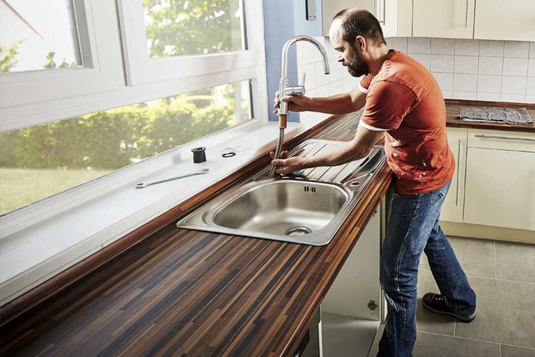 Installatie van een keukenkraan in een spoelbak op een werkblad met houten decor.