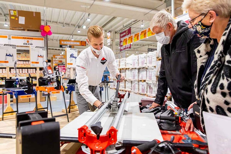 Demonstratie van een tegelsnijmachine in de winkel met twee toeschouwers