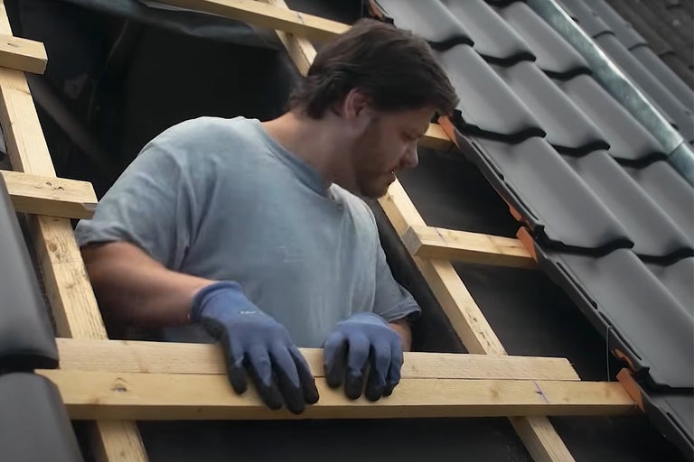 Een man werkt aan een dakconstructie met dakpannen.