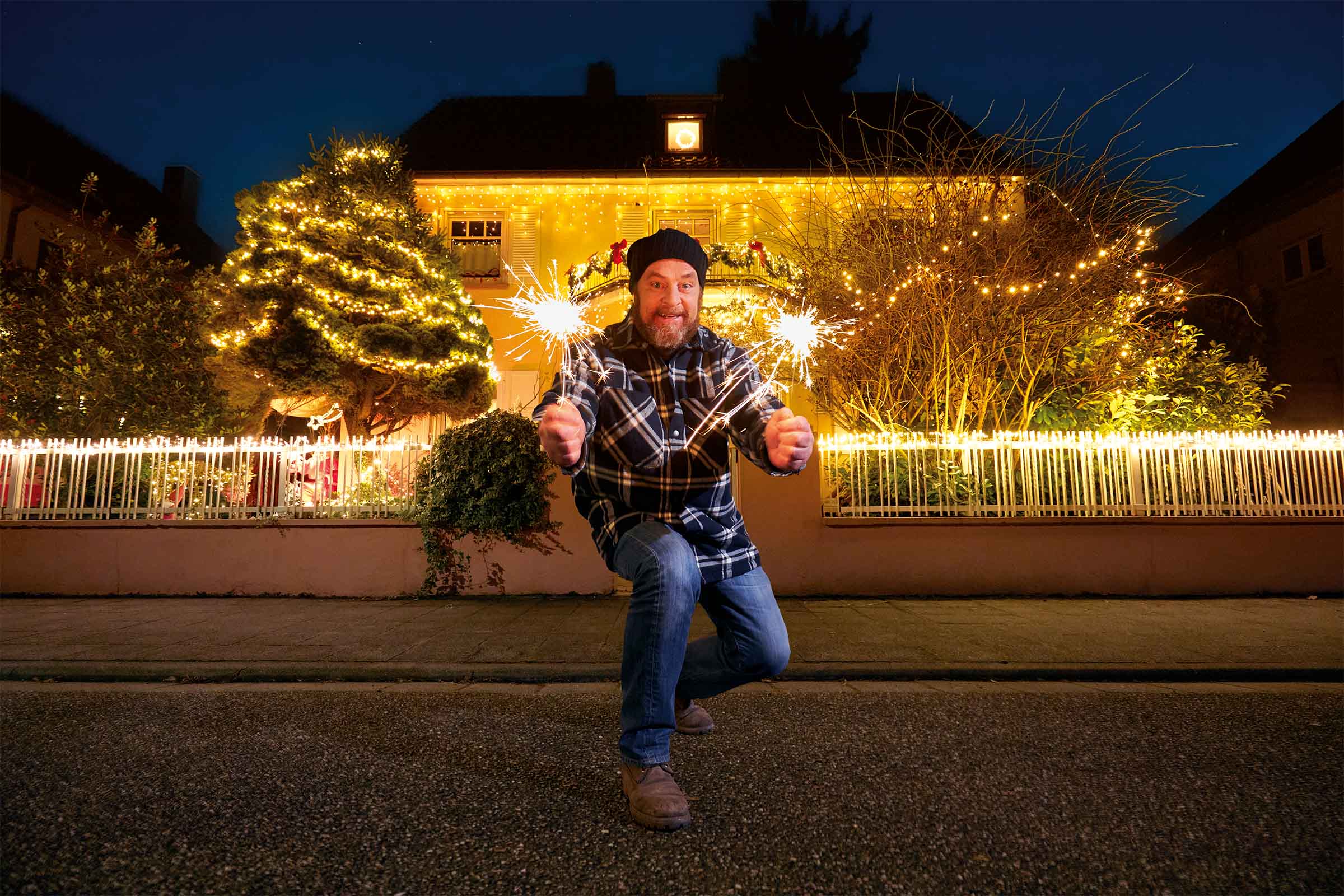 Man met sterretjes voor een huis met kerstverlichting