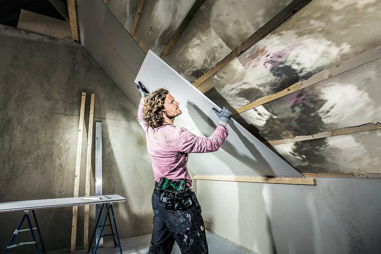 Een man monteert een gipsplaat op een zolder.