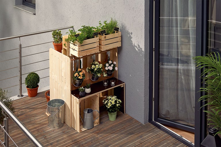 Houten rek met planten, emmer en gieter op een balkon.