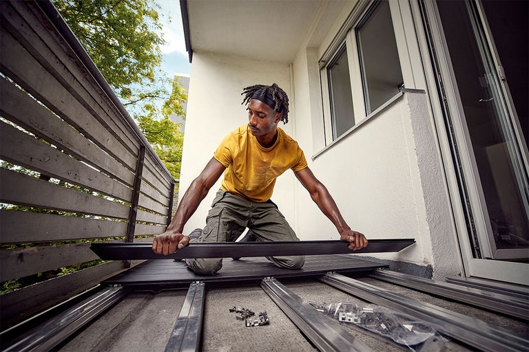 Man legt terrasplanken op een balkon. De terrasplanken zijn van hout en hebben een geribbeld oppervlak.