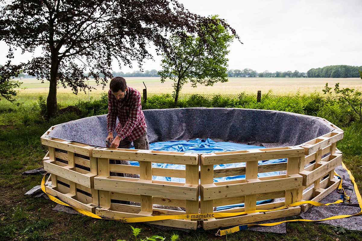 Man bouwt een rond zwembadframe van houten pallets in de tuin
