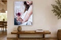 Schilderij op canvas in oliestijl van een vrouw met een glas rode wijn, hangend boven een houten bank in een lichte, moderne kamer.