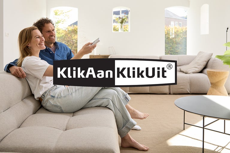Een paar ontspant zich op een bank in de woonkamer met het KlickAan KlickUit-logo.